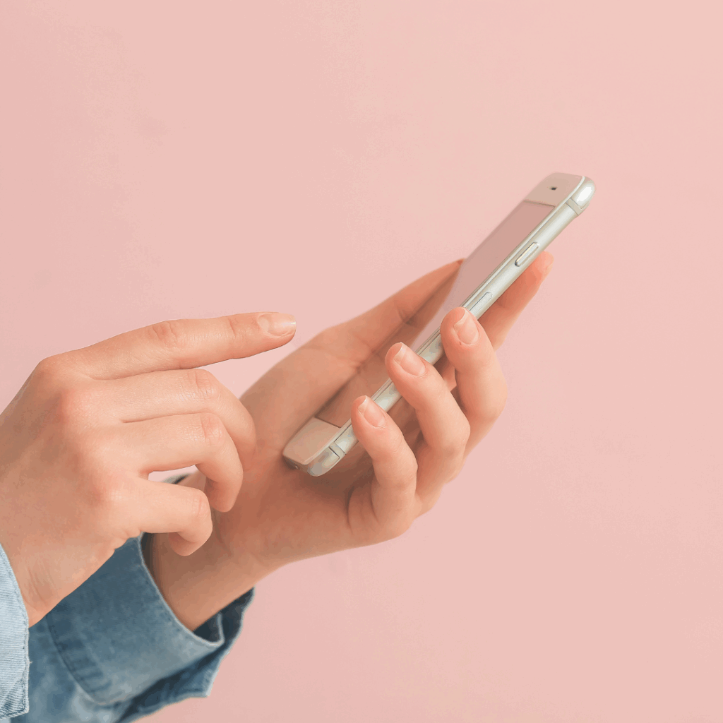 Close-up of a person texting on a smartphone with a soft pink background