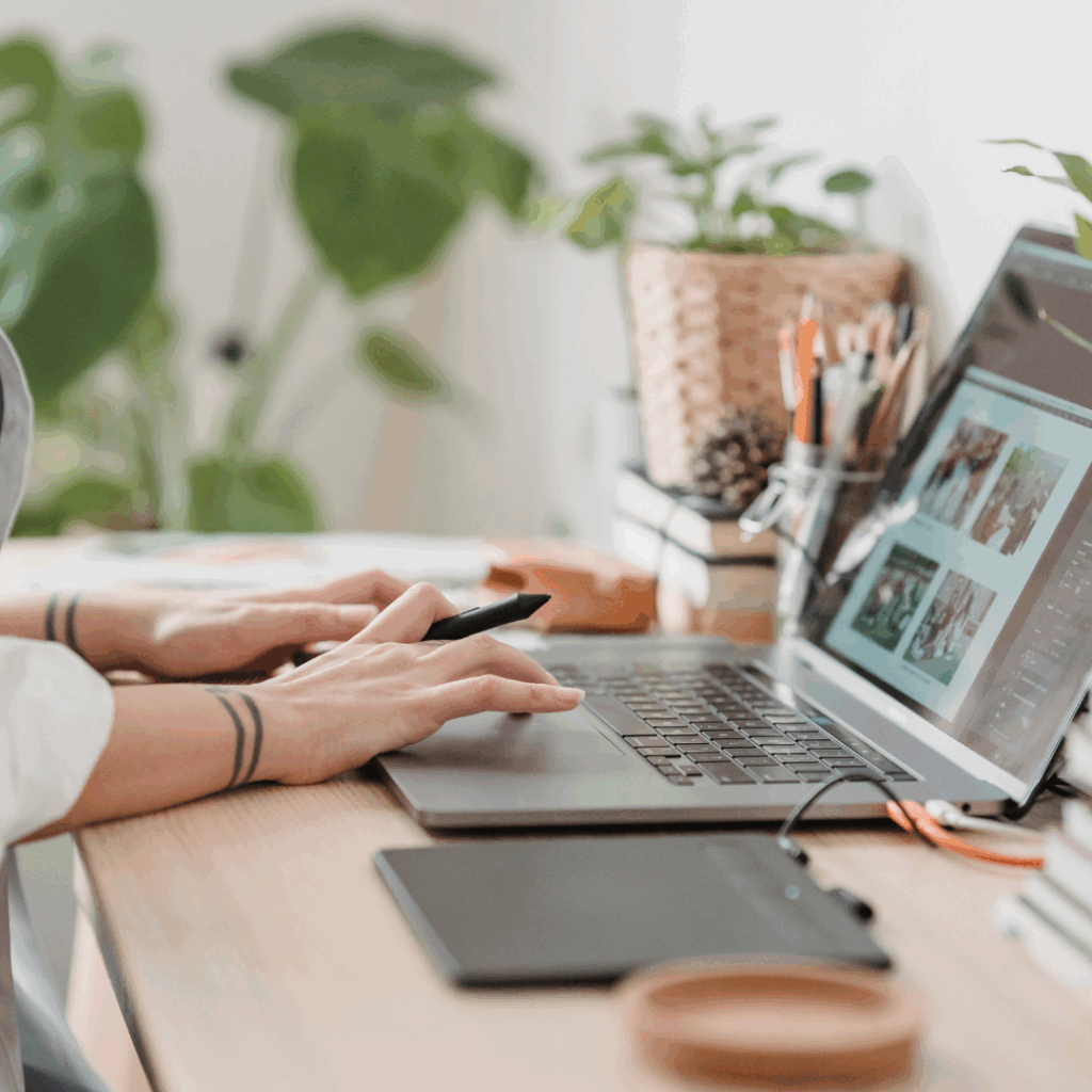 Person working on digital design at a laptop with image editing software and creative tools on desk