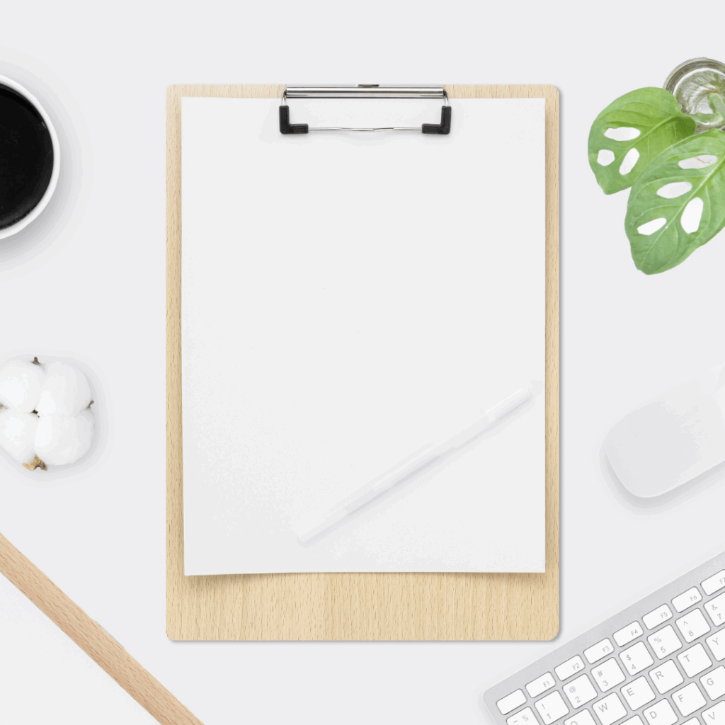 Minimalist flat lay with clipboard, pen, coffee, keyboard, and greenery on a white desk